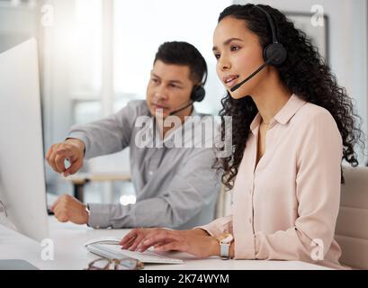 Understanding a few new processes. two call centre agents working together on a computer in an office. Stock Photo