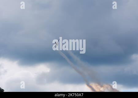 Plane climbing up with smoke at back within dark clouds Stock Photo
