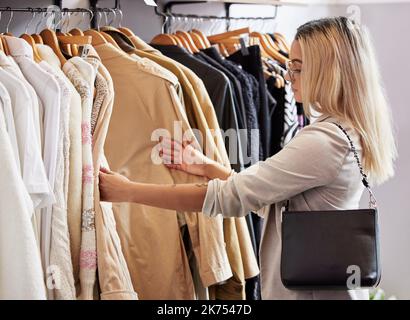 They have the best selection. a young woman browsing through clothing in a store. Stock Photo