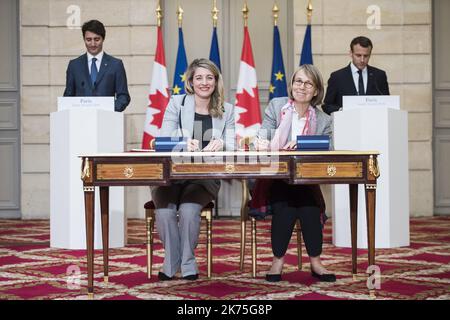 French President Emmanuel Macron (R) and Canadian Prime Minister Justin Trudeau (L) look as French Culture Minister Francoise Nyssen (2nd R) and Canadian Heritage Minister Melanie Joly (2nd L) sign an agreement at the Elysee Palace in Paris on April 16, 2018. Trudeau is on a two-day official visit to France.  Stock Photo