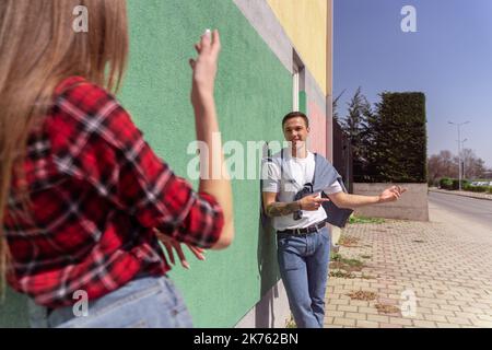Cute couple talking outside while leaning on the gren wall Stock Photo