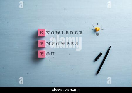 Knowledge empowers you sign written on blue wooden background with the first letter of each word on pink blocks. Light bulb made of yellow smashed pap Stock Photo