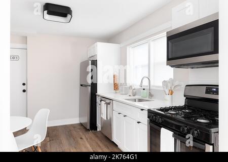 A cozy kitchen and dining room with white cabinets, stainless steel appliances and a white table and chairs. Stock Photo
