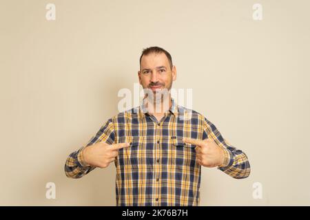 This is me. Portrait of man in plaid shirt pointing at himself and looking with arrogant and selfish expression, feeling successful and conceited Stock Photo
