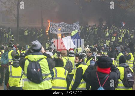 Demonstrators gather in front of a burning car during clashes with riot police as part of a protest of Yellow vests (Gilets jaunes) against rising oil prices and living costs on the Champs Elysees in Paris, France. Stock Photo