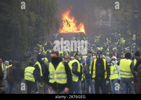 Demonstrators gather in front of a burning car during clashes with riot police as part of a protest of Yellow vests (Gilets jaunes) against rising oil prices and living costs on the Champs Elysees in Paris, France. Stock Photo