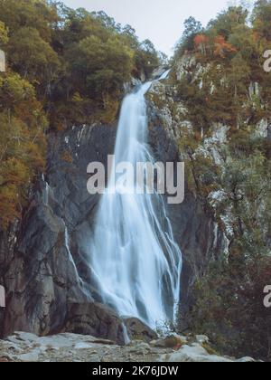 Long exposure tall waterfall surrounded by trees in autumn Stock Photo