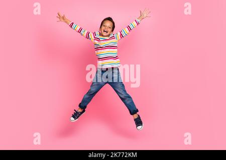 Full size photo of optimistic sweet nice boy wear striped long sleeve jeans jumping hands up screaming isolated on pink color background Stock Photo