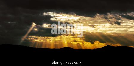 Rays of light shining through stormy clouds and covering dramatic sunset. Stock Photo