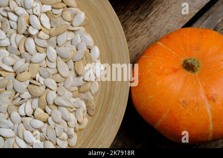 Pumpkins and pumpkin seeds in plate on wooden background Stock Photo