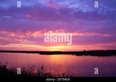 Beautiful sunset over the river. Magical sunrise behind colorful clouds over the lake. Calm water in a pond on the backdrop of a bright sky with Stock Photo