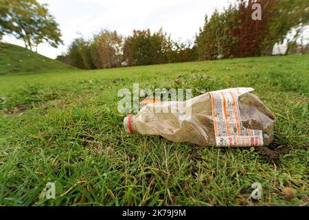 A low angle closeup on a transparent plastic garbage bottle laying on the green lawn in a public park Stock Photo
