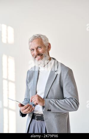 Smiling old senior businessman using tablet isolated on white wall, vertical. Stock Photo