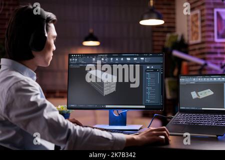 Male engineer working on industrial manufacture of technical engine product with infographics interface. Developing machinery component with engineering manufactory for science development. Stock Photo