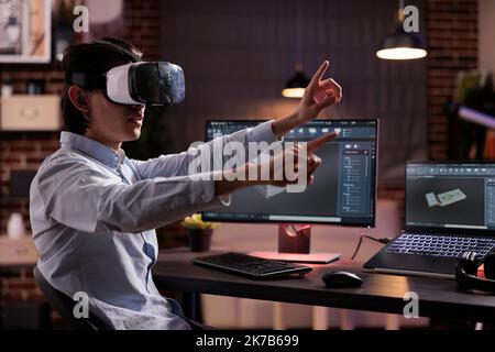 Male freelancer using vr glasses on industry production, engineering technical product with virtual reality headset and computer. Developing machinery engine component with cad software app. Stock Photo