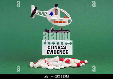 Medical concept. On a green surface, an ambulance helicopter, pills and a white sign with the inscription - Clinical Evidence Stock Photo