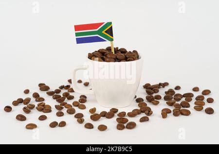 The flag of South Africa sticks out of a cup of roasted coffee beans. Concept of consumption and business. Stock Photo