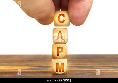 Business concept. A man puts wooden cubes on the table with the inscription - CAPM Stock Photo