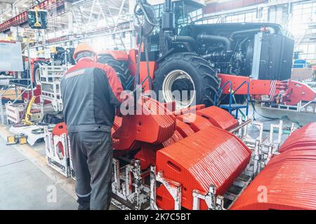Industrial worker assembles agricultural equipment in tractor or combine harvester production line in factory. Stock Photo