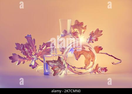 Biophilic Autumn background. Gilded gold maple leaves distorted by transparent glass jars, small bottles. Monocholored orange beige floral elements Stock Photo