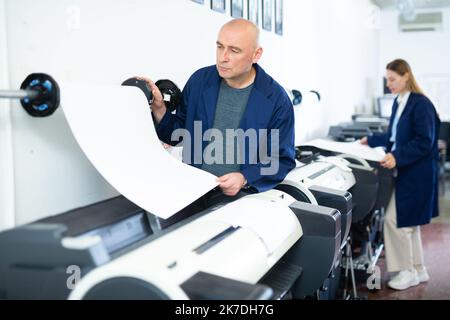 Service man uses plotter and checks functionality in printing shop Stock Photo