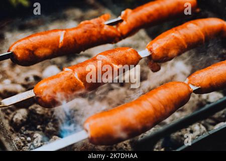 Sausages close-up on the grill on fire, against the background of smoke. Meat and snacks, food and fast food Stock Photo