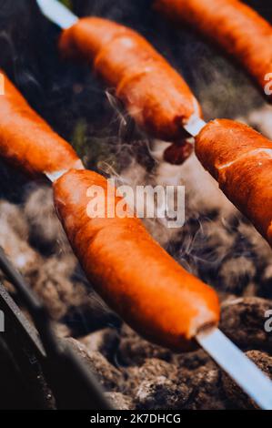 Sausages close-up on the grill on fire, against the background of smoke. Meat and snacks, food and fast food Stock Photo
