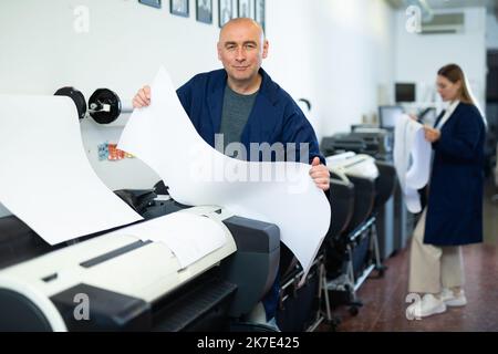 Service man uses plotter and checks functionality in printing shop Stock Photo