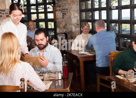 Guests of the country restaurant discuss menu with waitress Stock Photo