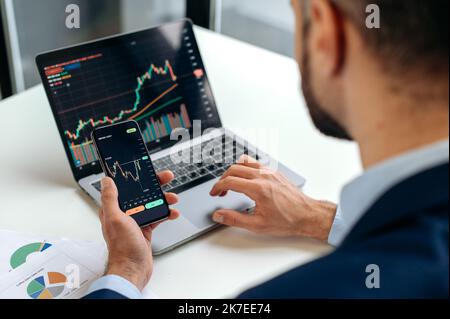 Close-up of male hands holding smartphone. Trader investor analyst using mobile phone app for cryptocurrency stock market, analyzing graph trading data index investment growth chart, plans strategy Stock Photo