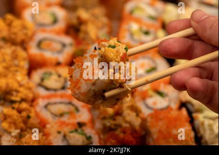 Someone takes a chopsticks roll from a set of different types of rolls in a box. Top view of various portions of vegetarian and fish rolls. Close-up, Stock Photo