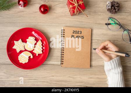 Woman hand writing 2023 PLANS on notebook with Christmas cookies on table. Xmas, Happy New Year, Goals, Resolution, To do list, and Strategy concept Stock Photo