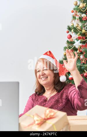 Mature Hispanic woman greeting her loved ones via video call during Christmas using her laptop. Concepts: the joy of sharing during the holidays, the Stock Photo