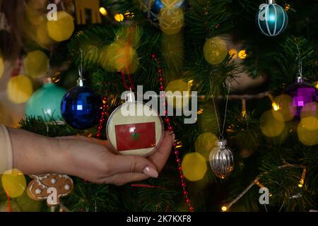 a girl holds a decoration on a fir tree with the flag of Morocco Stock Photo