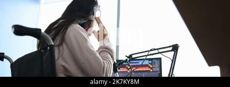 Woman in wheelchair with headphones in front of microphone and computer Stock Photo
