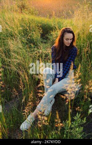 Portrait of a beautiful young woman on meadow watching the sunset enjoying nature summer evening outdoors. Stock Photo