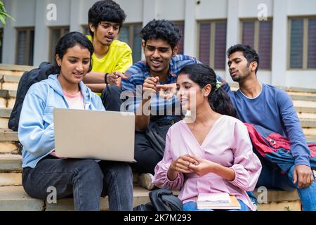 Group of happy students checking results on laptop while sitting on college campus - concept of education, technology and project work discussion. Stock Photo
