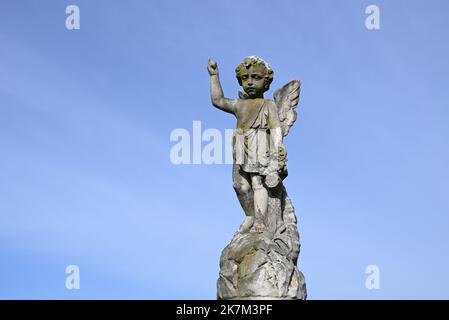 Cherub, or child angel, sculpture made of stone, pointing towards the heavens with blue sky in the background Stock Photo