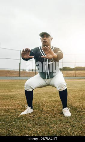 Baseball player, stretching and sports man doing squats on field for warm up exercise, workout and practice for match. Male athlete with tshirt and Stock Photo