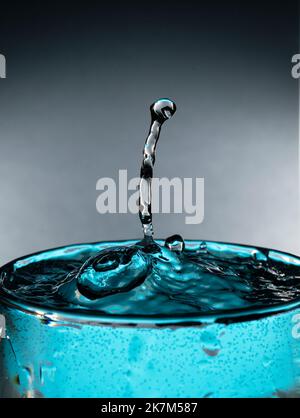 Water drop splash in a glass cup blue colored. Stock Photo