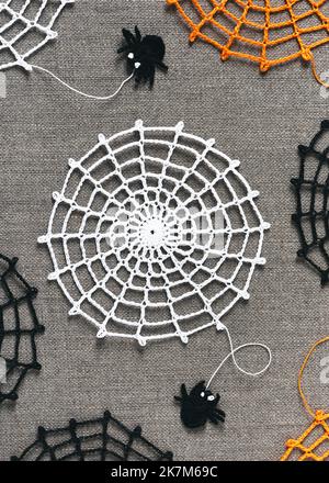 White crochet spider web on nature linen background with small funny black spaders. Halloween autumn decoration and easy handmade concept. Flat lay Stock Photo