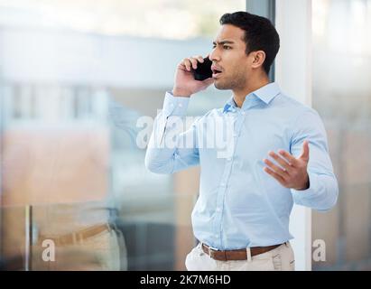 Why would you do this now. a young businessman looking angry while making a phone call using his smartphone. Stock Photo