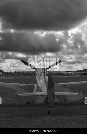 black and white picture in portrait format of a spitfire parked on grass with dark clouds in the sky, would suit book cover Stock Photo