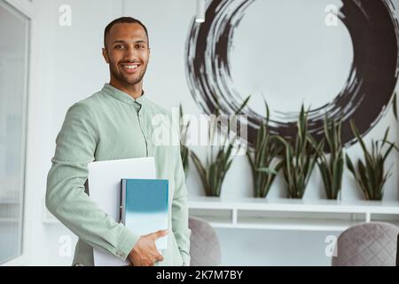 Smiling african businessman standing in modern office and holding laptop Stock Photo