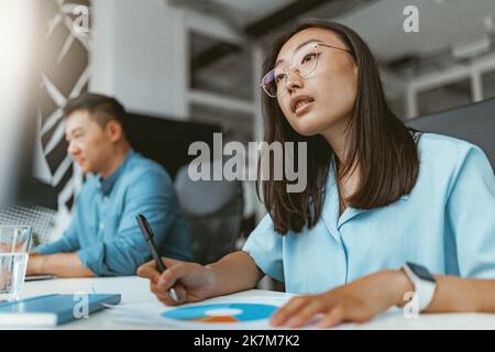 Smiling asian businesswoman working with documents sitting in coworking on colleagues background Stock Photo