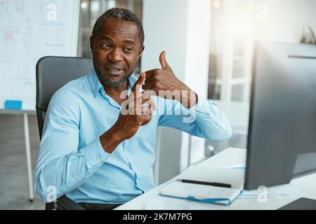 African businessman using sign language while talking online with client sitting in office Stock Photo