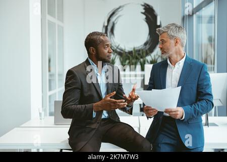 Two businessmen talking about deal sitting in meeting room in modern office Stock Photo