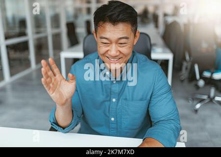 Smiling asian businessman talking online with client sitting in office Stock Photo