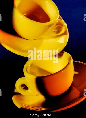 Bright illuminated yellow cups with saucer in dark blue back Stock Photo