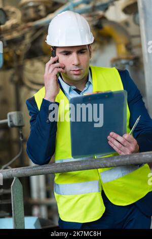 male engineer in factory holding clipboard and talking on telephone Stock Photo